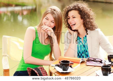 Two Beautiful Women Laughing Over A Cofee At The River Side Terrace