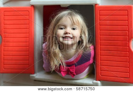 Little blond girl smiling through the window of kids playhouse