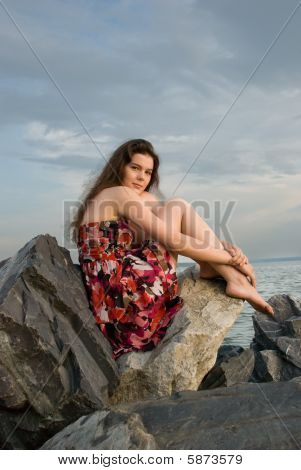 Menina sentar-se na rocha na costa do mar