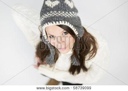 Adorable young girl in warm winter pullover and grey cap, looking up with a cute smile on her face, isolated on grey background.