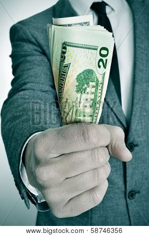 a man wearing a suit sitting with a wad of american dollar bills in his hand