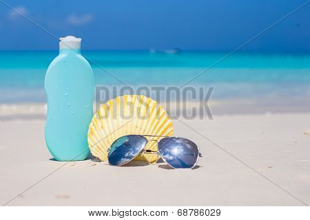 Bottle of suncream, sunglasses and shell on the white beach