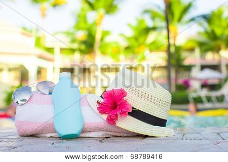 Suncream, hat, sunglasses, flower and tower near pool