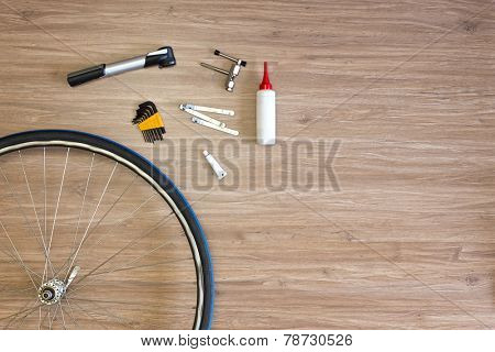 Background with bicycle tools laid out on a wooden floor, with a spoked wheel, tire levers, a pump, glue and a chain punch. Items, used to repair a flat tire