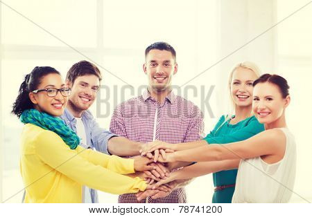 business, office, gesture and startup concept - smiling creative team with hands on top of each other sitting in office