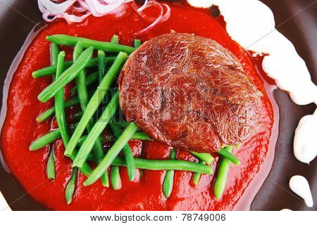 pork medallion served on tomato sauce with green peas on dark plate isolated on white background
