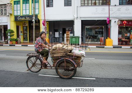 Old woman in bare feet transports folded cardboard boxes with an old bicycle