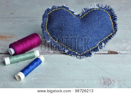 Denim heart and thread on wooden background
