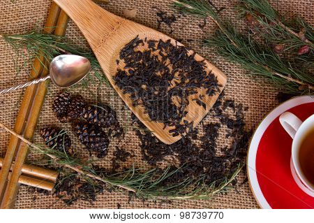 Shot From The Dry Black Tea With Pine Branches , A Teaspoon Against A Background Of Burlap