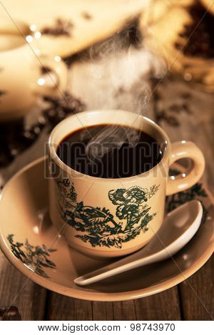 Steaming traditional oriental Chinese kopitiam style dark coffee in vintage mug and saucer with coffee beans. Fractal on the cup is generic print. Soft focus with dramatic light on wooden background.