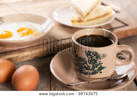 Steaming traditional oriental Chinese kopitiam style dark coffee in vintage mug and saucer with coffee beans. Fractal on the cup is generic print. Soft focus with dramatic light on wooden background.