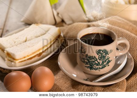 Steaming traditional oriental Chinese kopitiam style dark coffee in vintage mug and saucer with coffee beans. Fractal on the cup is generic print. Soft focus with dramatic light on wooden background.