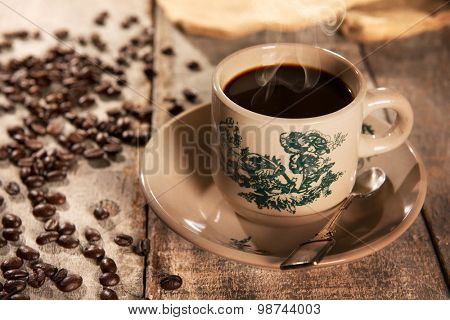 Steaming traditional oriental Chinese kopitiam style dark coffee in vintage mug and saucer with coffee beans. Fractal on the cup is generic print. Soft focus with dramatic light on wooden background.
