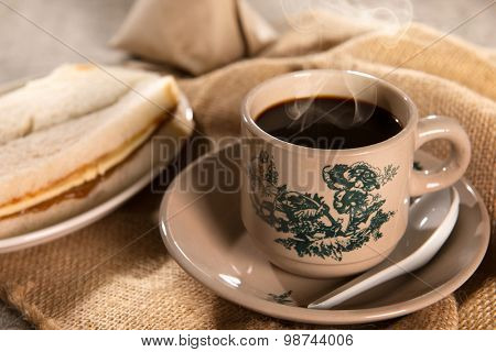 Steaming traditional oriental Chinese kopitiam style dark coffee in vintage mug and saucer with coffee beans. Fractal on the cup is generic print. Soft focus with dramatic light on wooden background.