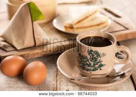 Steaming traditional oriental Chinese kopitiam style dark coffee in vintage mug and saucer with coffee beans. Fractal on the cup is generic print. Soft focus with dramatic light on wooden background.
