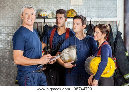 Portrait of happy mature fireman standing with team at fire station