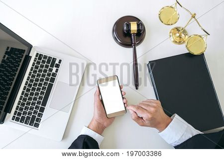 Male lawyer or judge working with smart phone and scales of justice Law book gavel report the case on table in modern office Law and justice concept. Top view.