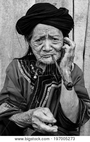 2010-07-25 in Phongsali, Laos: portrait of old hill tribe woman in traditional clothes smoking a pipe