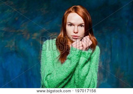 young pretty cold redhead girl in greem pullover over dark blue background. beauty model woman with luxurious red hair. hairstyle. holiday makeup
