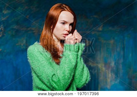 young pretty cold redhead girl in greem pullover over dark blue background. beauty model woman with luxurious red hair. hairstyle. holiday makeup