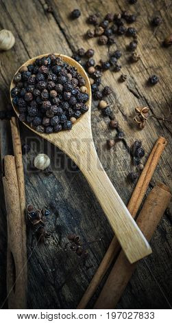 Black pepper seeds in spoon on old wooden floor.