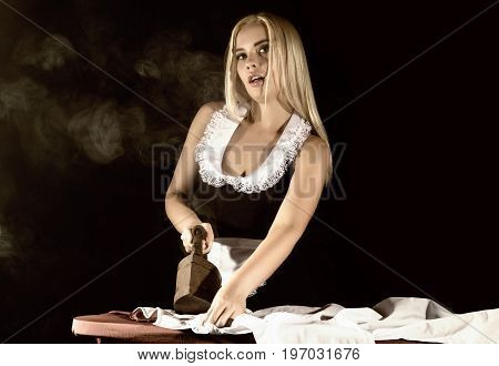 sexy blonde woman in housekeeper suit, ironing white shirt with old iron. retro style. housewife concept
