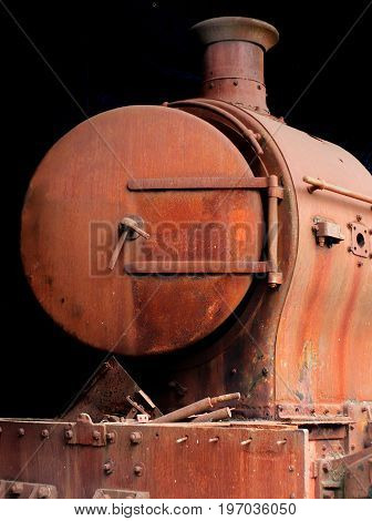 old rusting abandoned steam locomotive from the front showing door buffers and chimney on a black background