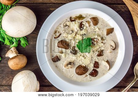 An overhead photo of a plate of a mushroom cream soup with champignons, cremini, and fresh parsley, with grated cheese