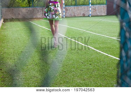 Young attractive woman on the soccer field behind the damaged metal mesh fence.