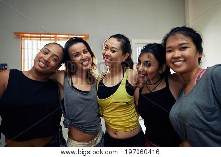 Waist-up group portrait of smiling women posing for photography while gathered together in modern dance hall for intensive training