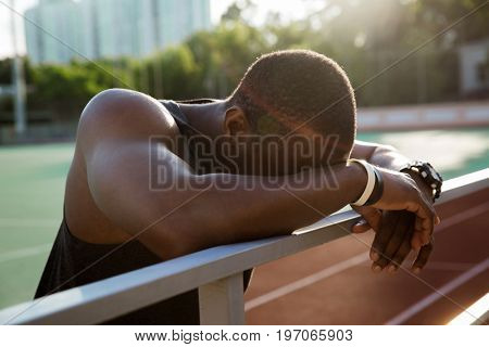 Close up of a tired african sportsman leaning on the railing and resting after workout at the stadium
