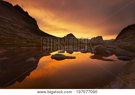 Sunset in mountains near lake. Sunlight reflected on mountain tops. Golden light from sky reflected in a mountain lake. Ergaki