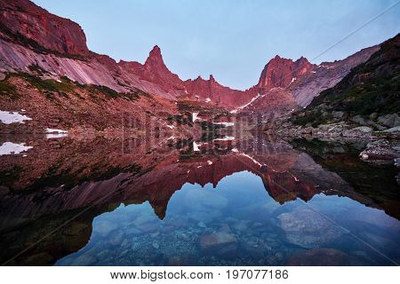 Sunset in mountains near lake. Sunlight reflected on mountain tops. Golden light from sky reflected in a mountain lake. Ergaki
