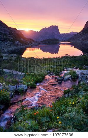 Sunset in mountains near river. Sunlight reflected on mountain tops. Golden light from sky reflected in a mountain river. Ergaki