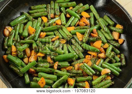 Blackened stir fry green beans and carrots in cast iron frying pan skillet