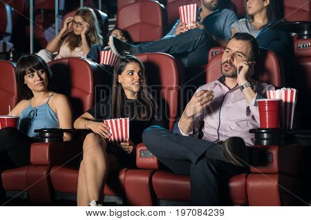 Hispanic man being disrespectful by talking on the phone at the movie theater next to some annoyed neighbors