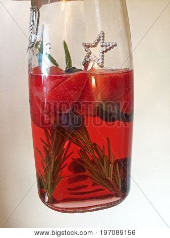 Jug of summer cocktail with strawberries, rosemary and blueberries