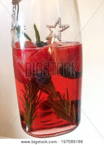 Jug of summer cocktail with strawberries, rosemary and blueberries