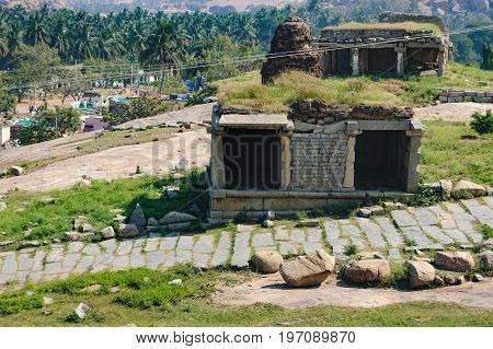 View of ancient ruins on Hemakuta hill in Hampi, Karnataka, India. Landscape with unique mountain formation Hampi Village in the distance tropical nature and the road along temple.