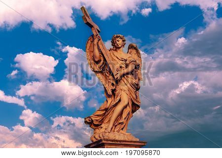 Marble statue of Angel with the Cross at sunset, one of the ten angels on Saint Angel Bridge, symbols of Christ's Passion, Rome, Italy