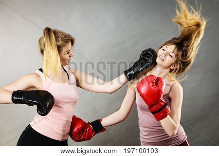 Two agressive women wearing boxing gloves having argue fight being mad at each other. Female violance concept.