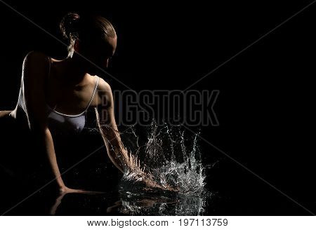 Young beautiful blonde with bunch hair style wearing white top enjoying water splashes in dark studio