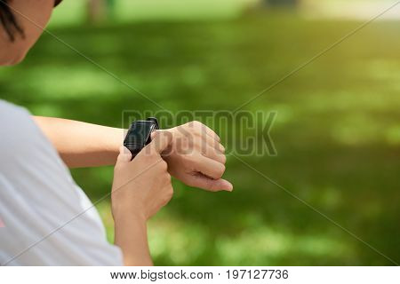 Closeup image of young woman checking fitness watch on wrist during workout outdoors