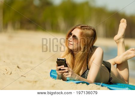 Summertime pleasures enjoying vacation concept. Woman in bikini sunbathing and relaxing on beach using smartphone checking social media and writing sms