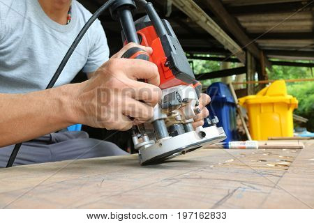Asian workers using electric routering to cut down stripes on the wood.