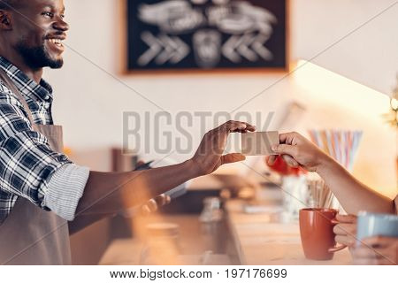 Handsome Smiling African American Barista Taking Credit Card For Payment On Bar Counter In Cafe