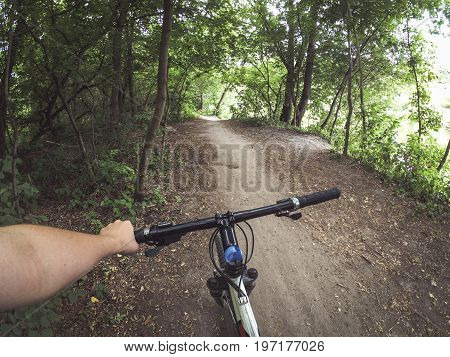 A man cyclist holds a bicycle behind the wheel with one hand in the woods. Copy space.