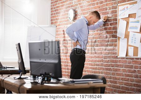 Businessman Leaning Against The Brick Wall Having Back Pain In Office