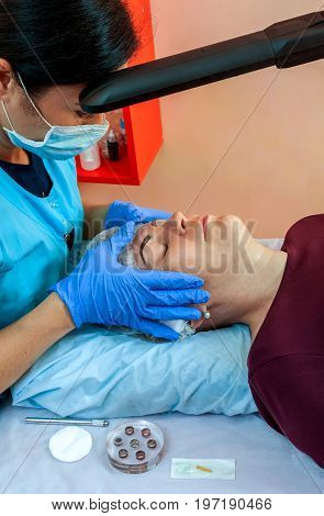 Correction of the shape of the eyebrows with permanent make-up. The cosmetologist at work.