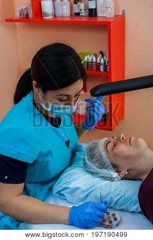 The cosmetologist performs correction of the shape of the eyebrows in the beauty salon. Semi-permanent makeup for eyebrows.